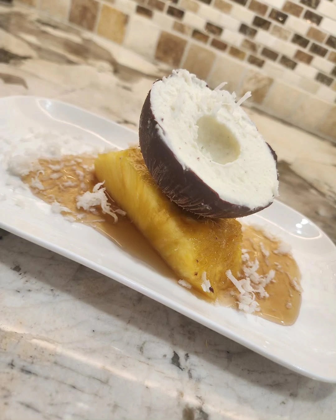 Coconut Mousse and Bourbon Mousse inside Chocolate Shell served on sweet pineapple glazed in brown sugar syrup.png Coconut Mousse and Bourbon Mousse inside Chocolate Shell served on sweet pineapple glazed in brown sugar syrup.png