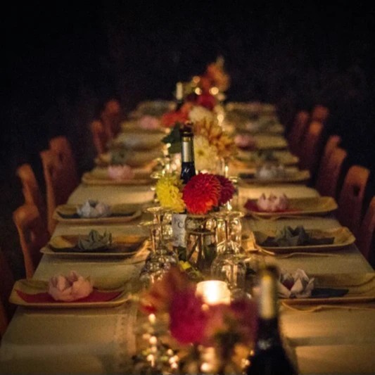 An elegant candle lit dinner table for twenty with flower decorations and folded colorful napkins