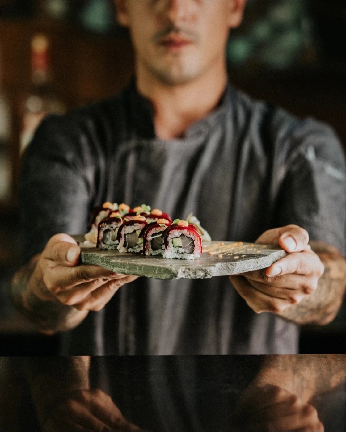 Tatooed chef hands slicing through a large piece of tuna on the cutting board