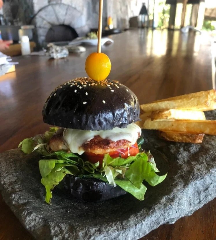 Bbq burger with charcoal black buns and chicken patty with thick fries served on a rustic rock plate
