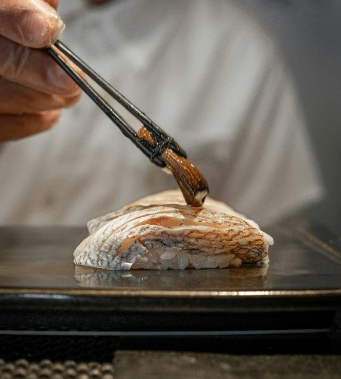 A chef squeezes ginger roots over a chu toro nigiri on a cutting board