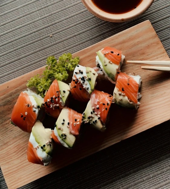 Salmon maki rolls with sesame seeds sprinkled and garnished with curly lettuce on a cutting board