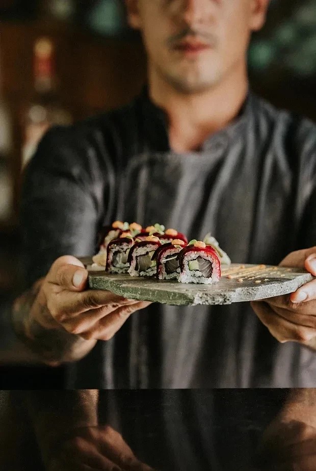 Tatooed chef hands slicing through a large piece of tuna on the cutting board