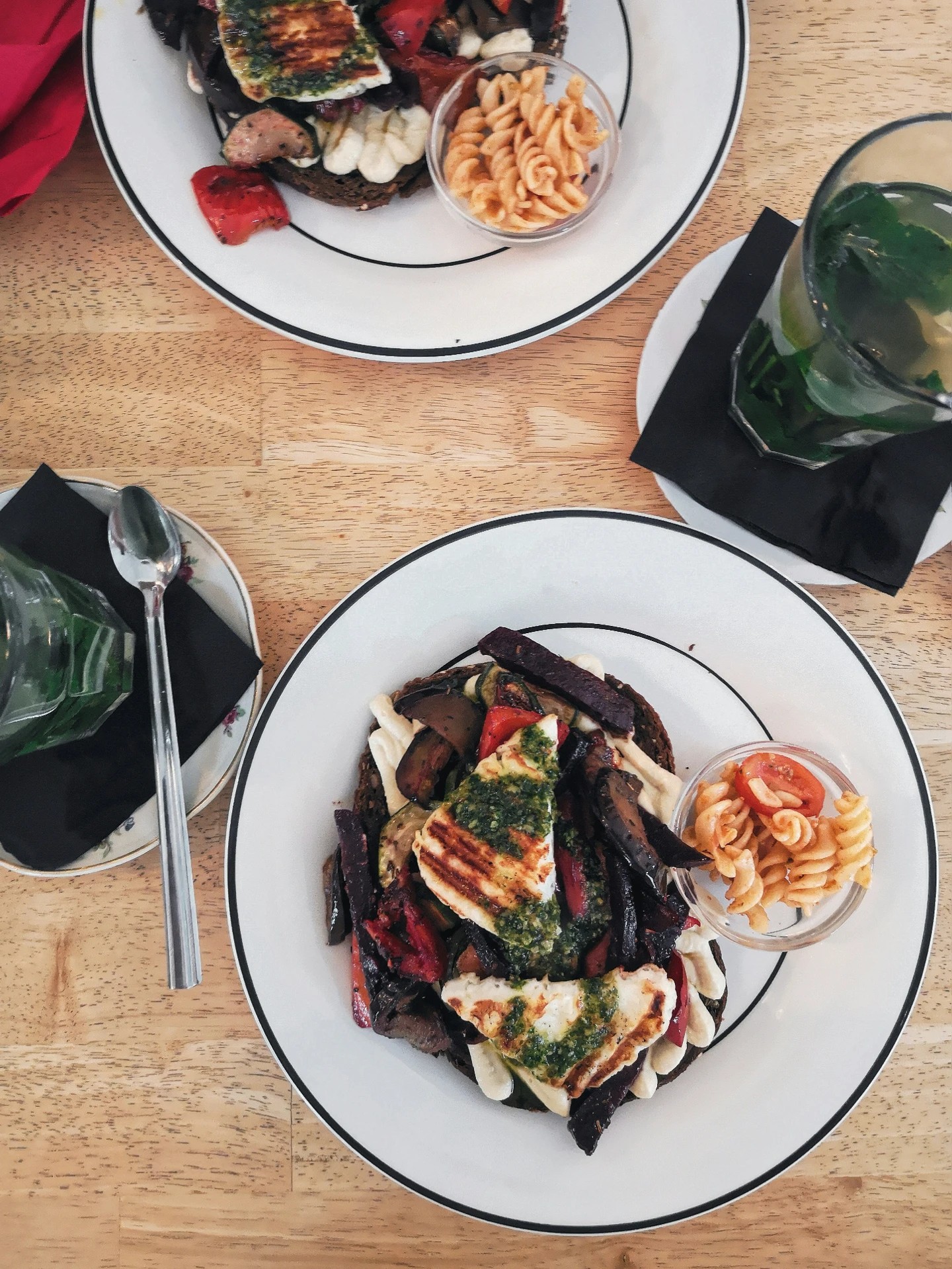 Top view of a gourmet grilled vegetable platter with halloumi cheese, pesto drizzle, and a side of pasta salad, ideal for showcasing a private chef BBQ party menu.