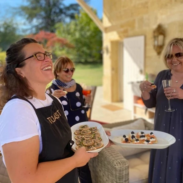 Smiling chef holds two plates with appetizers for her guests to enjoy al fresco