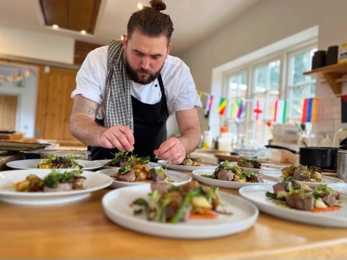 Chef squirting oil on hibachi vegetable and a flame rising from the grill