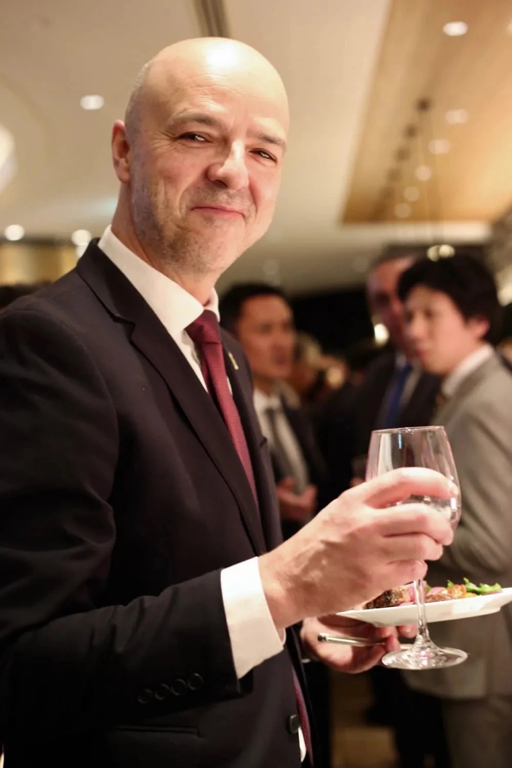Well dressed smiling man holding an appetizer and a glass in the middle of an formal company event