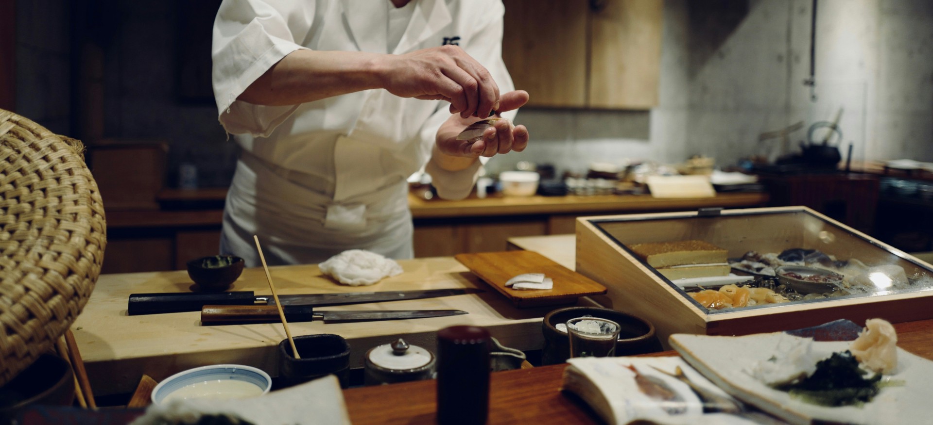 A chef squeezing lemon on a sashimi slice over the counter table where all his utensils are laid down