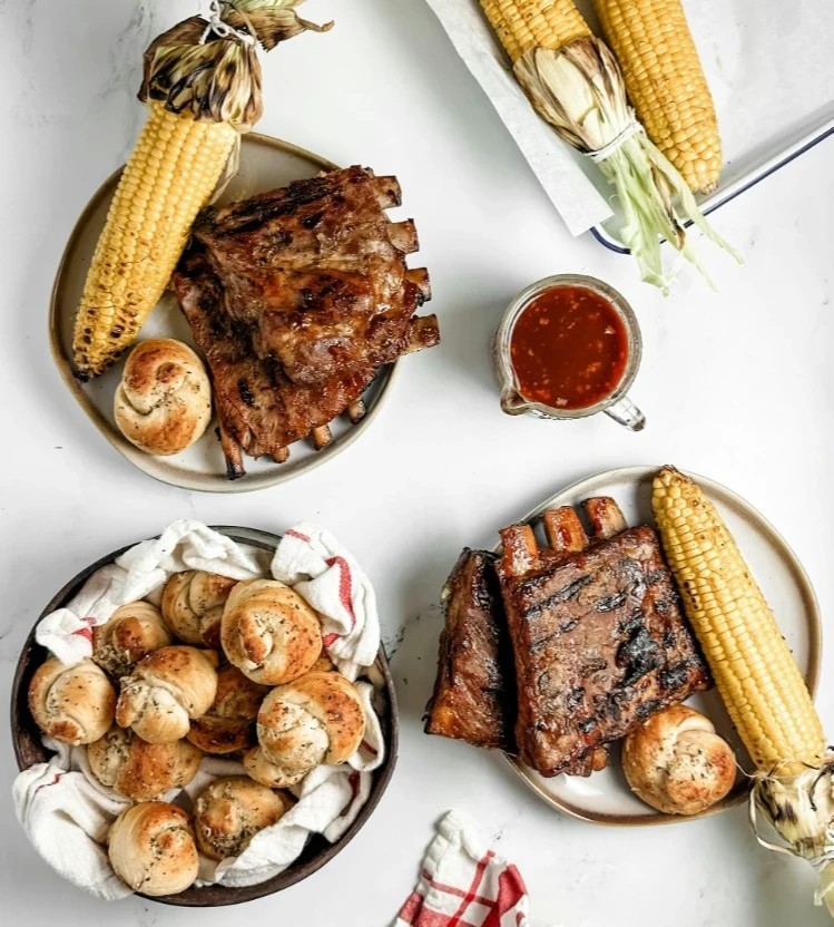 Racks of ribs basted in bbq sauce served with bread rolls and grilled corn on the cob