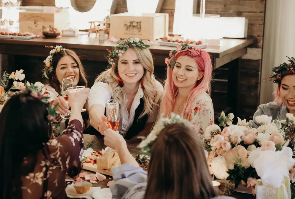 A group of women with flower crowns raise their glasses to toast at a bachelorette party