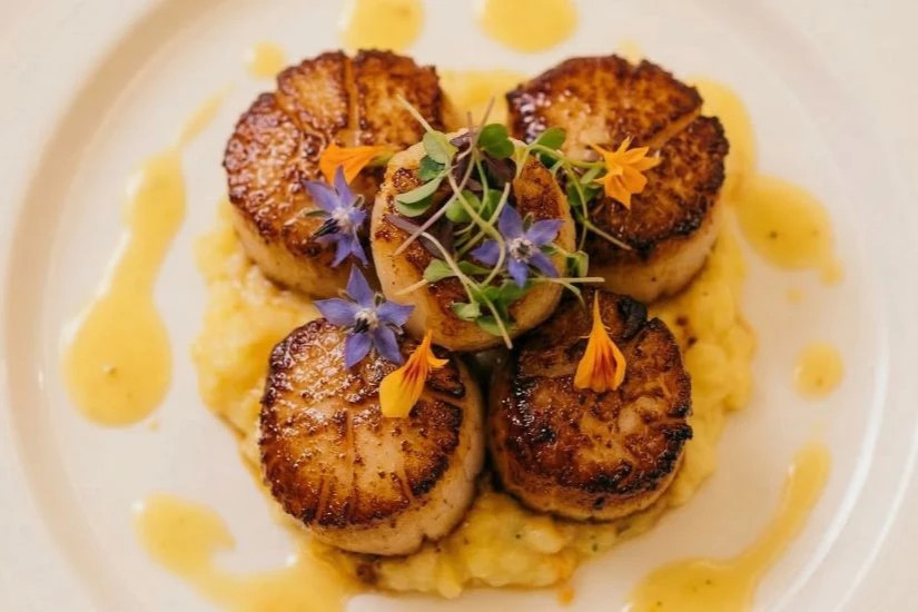 Four perfectly pan-seared scallops, golden brown on the top and bottom with a white tender center