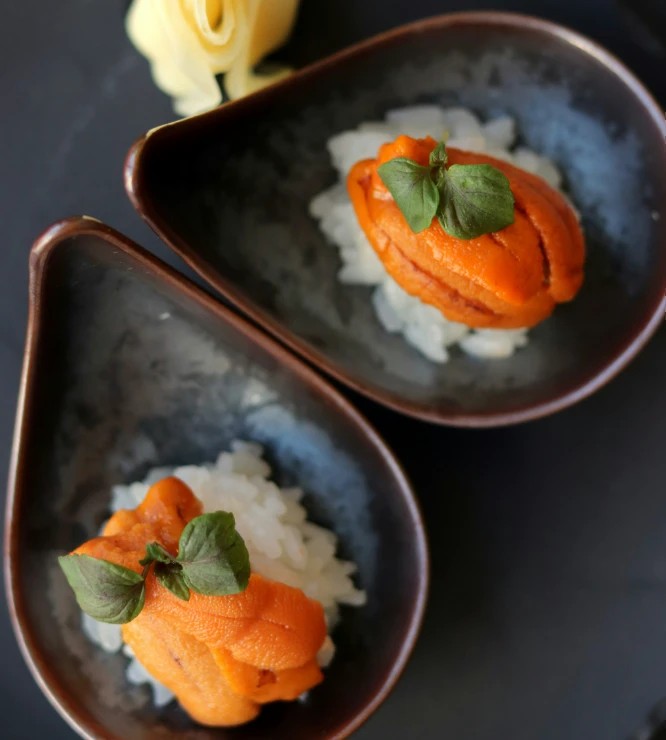 Two sumeshi balls topped with cream of salmon and basil leaves in ceramic bowls shapped like dropplets